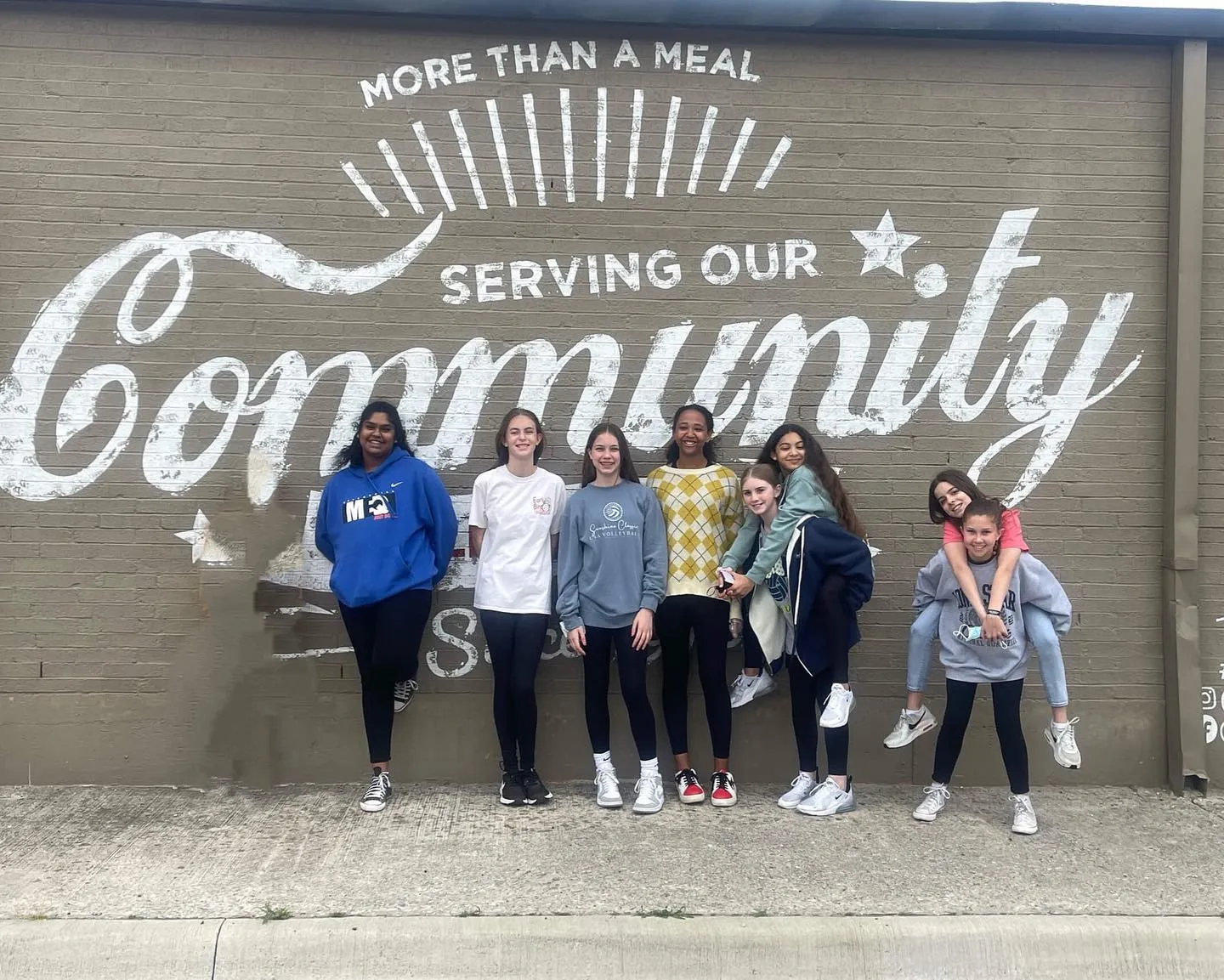 Young volunteers in front of a “Serving our Community” mural