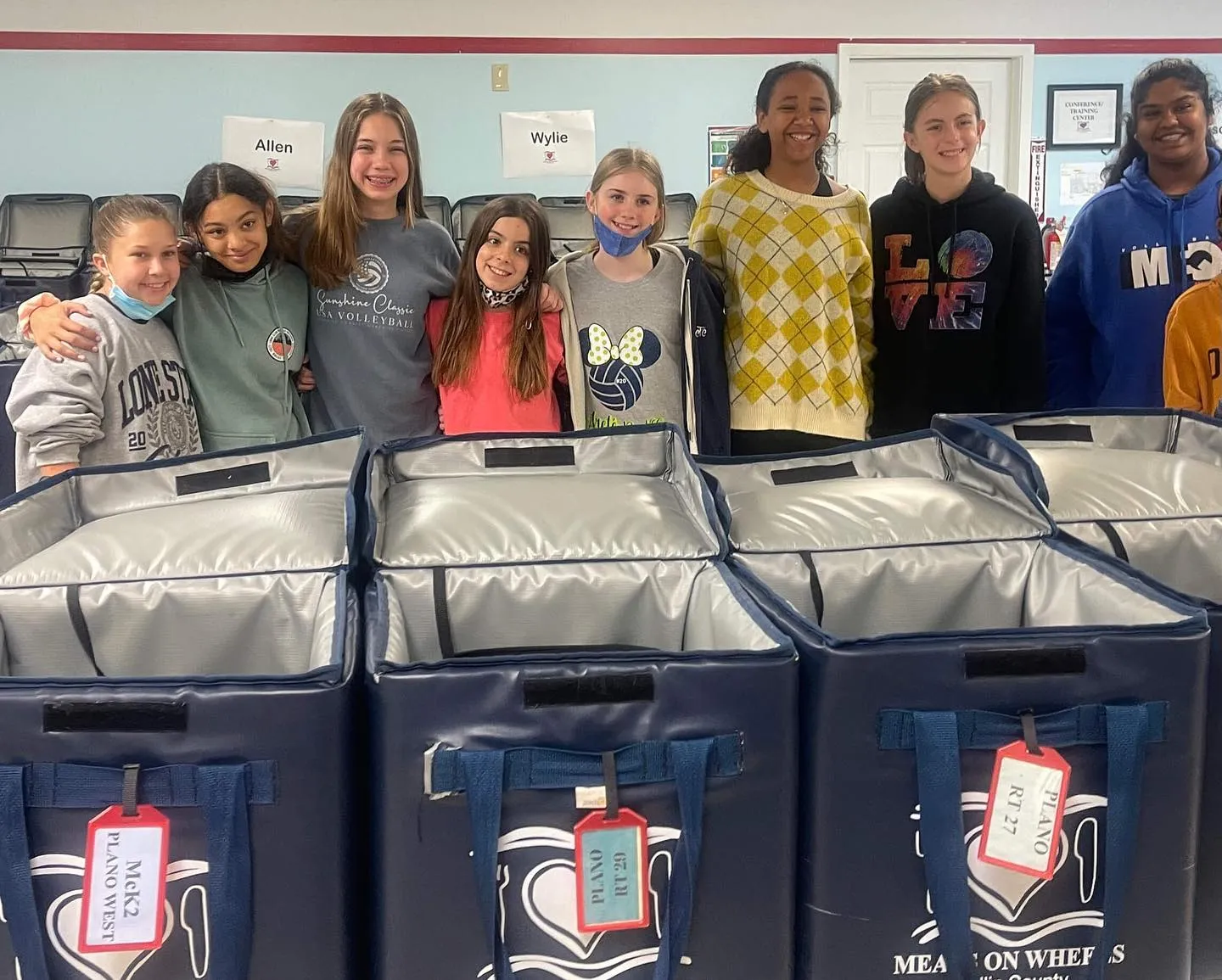 Smiling girls stand behind open insulated Meals on Wheels delivery bags