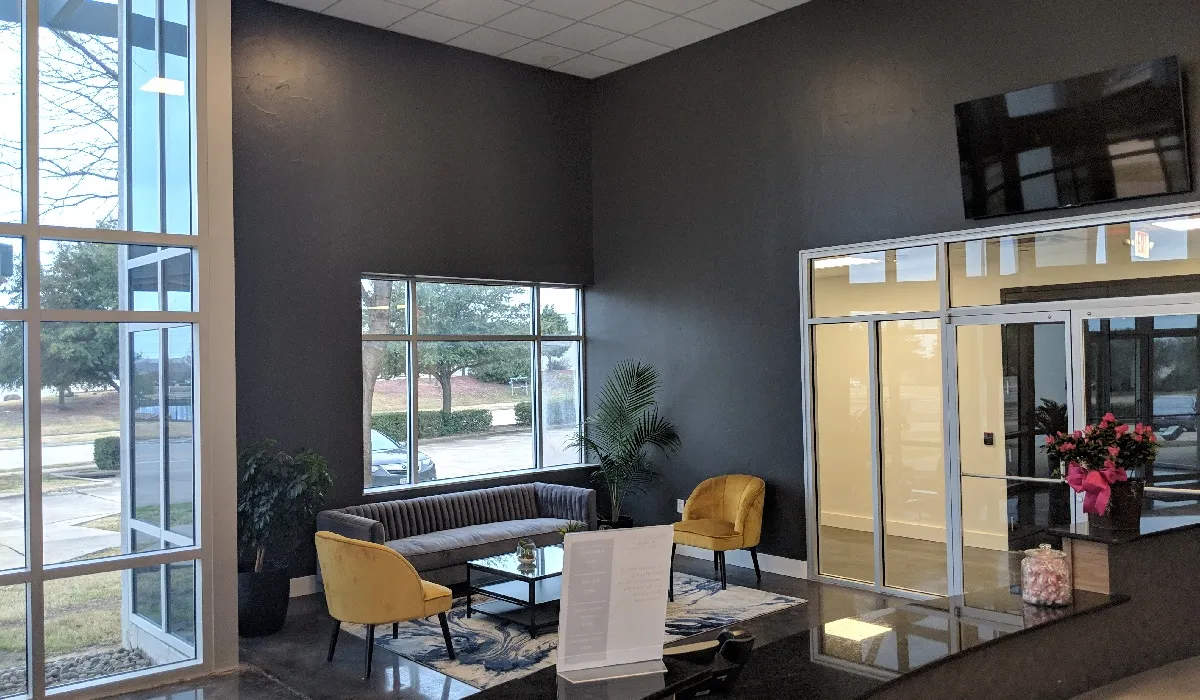 The WorkSpaces lobby with a dark feature wall, wall-mounted TV, sofa and yellow armchair beside tall windows