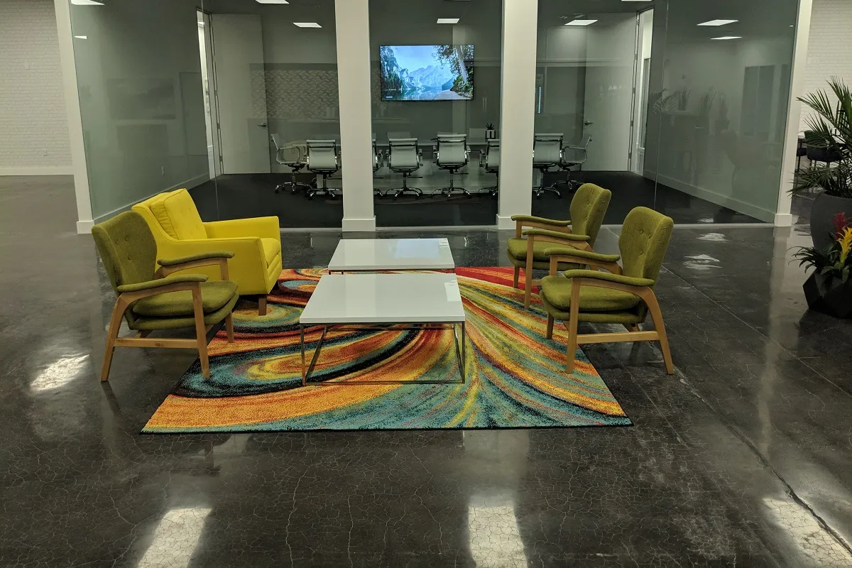 Green armchairs and a white coffee table on a colourful rug in front of a glass-walled conference room