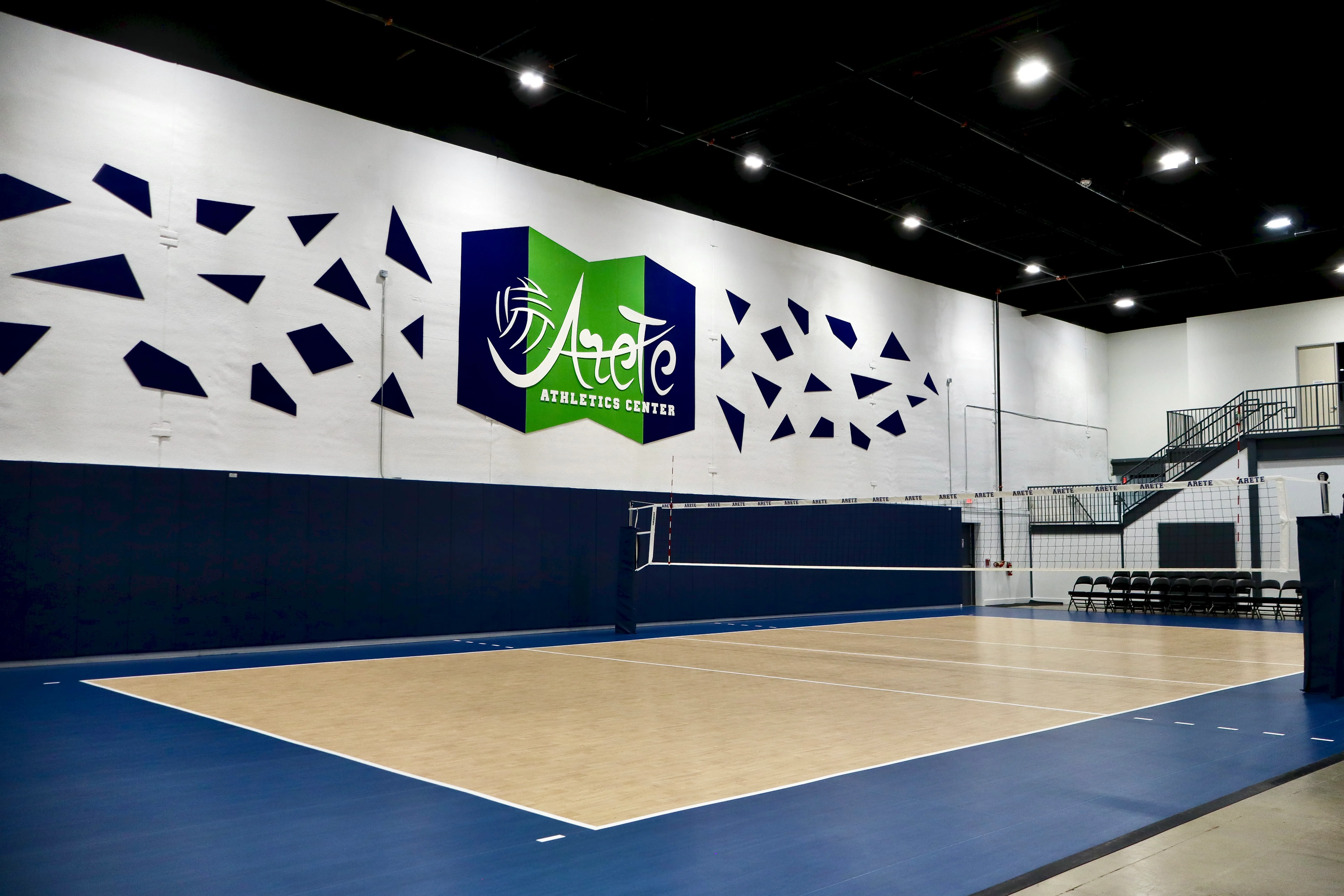 An Areté volleyball court in front of the Areté Athletics Center wall graphic